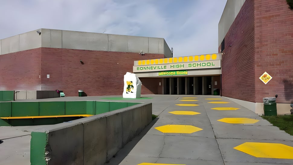 Se ve el edificio de la Bonneville High School con un camino amarillo y verde hacia la entrada y un patio pavimentado.