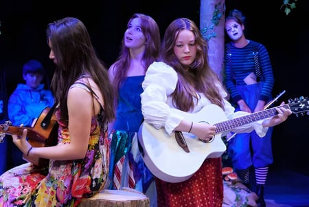 Un grupo de jóvenes mujeres de Bootham School actúa con instrumentos musicales en un escenario con iluminación colorida.
