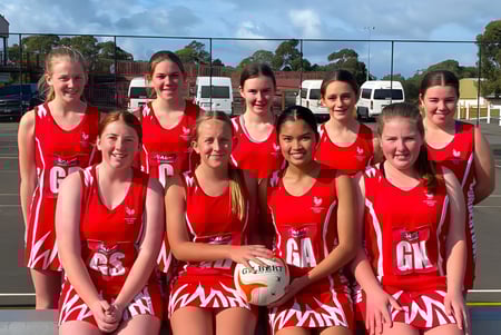 Un grupo de jóvenes jugadoras de netball con camisetas rojas está reunido en el campo al aire libre de Bordertown High School.