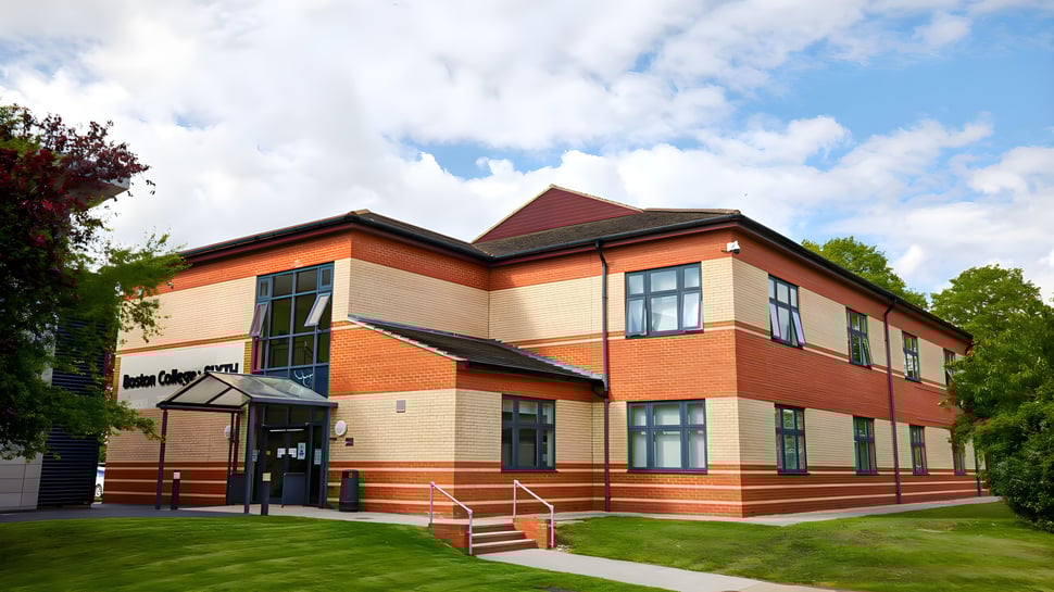 El edificio de ladrillo de dos pisos con techo rojo en el campus del Boston College está rodeado de césped y árboles.
