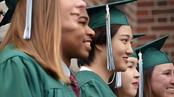 Graduados de la Boston Trinity Academy están juntos en togas y birretes verdes y sonríen.