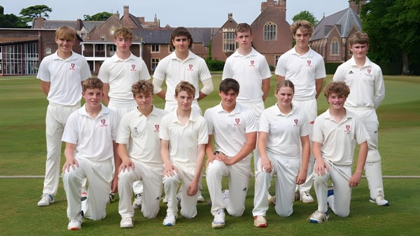 Un grupo de estudiantes en uniformes de cricket posan en un campo de césped frente a un edificio histórico en el campus del Bosworth Independent College.