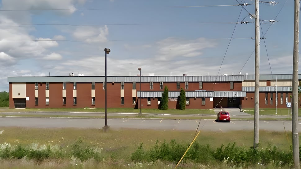 El edificio de ladrillo de varios pisos de Botwood Collegiate, con un auto rojo en primer plano, está rodeado de un prado.