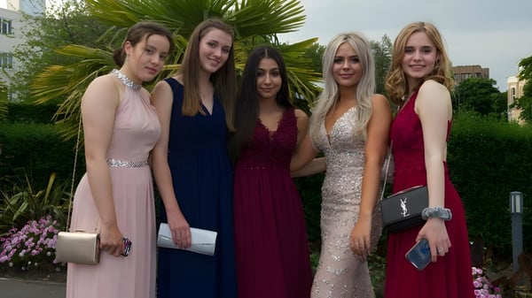 Cinco alumnas de Bournemouth Collegiate School posan con ropa formal frente a un fondo de plantas tropicales.