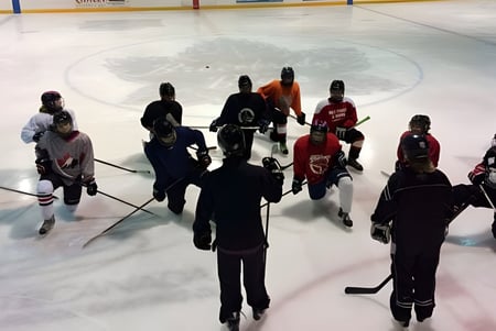 Estudiantes de la Bracebridge and Muskoka Lakes Secondary School están en diferentes camisetas sobre el campo de hielo con un gran logo en el centro.