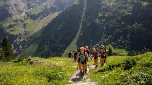 Un grupo de estudiantes del Bradfield College camina a través de un paisaje montañoso con densos bosques de fondo.