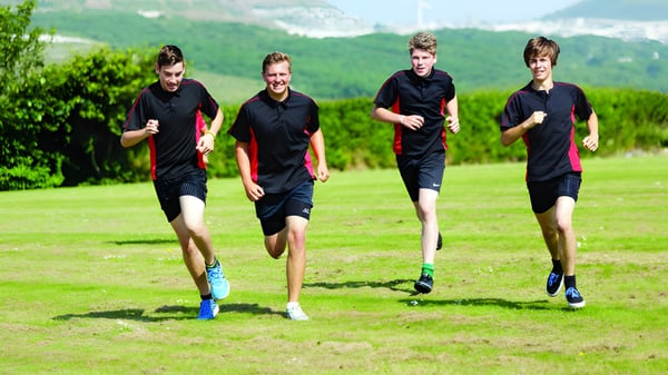 Cuatro estudiantes de la Brannel School corren en un campo cubierto de hierba con montañas al fondo.