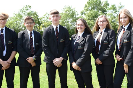 Un grupo de estudiantes de la Brannel School está de pie con ropa formal en un prado con árboles al fondo.