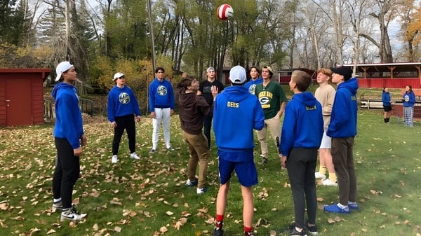 Un grupo de estudiantes de la Brant Christian School lleva uniformes azules y está de pie en un área boscosa con hojas en el suelo.