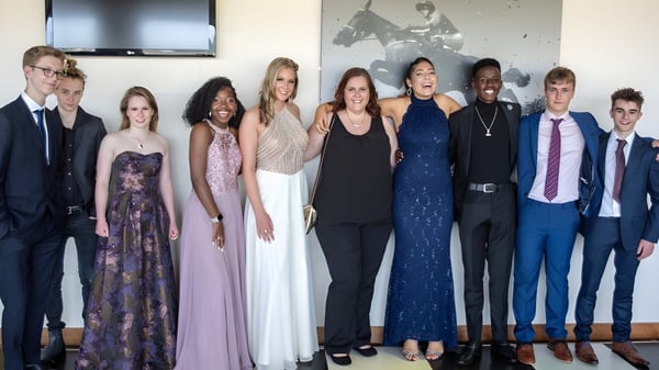 Un grupo de personas con ropa formal está frente a una pared decorada en el terreno de la Bredon School.