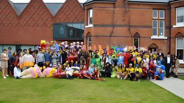 Un grupo de estudiantes de la Brentwood School en coloridos disfraces reunidos frente a un edificio histórico de ladrillo.