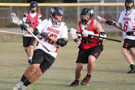Un grupo de jugadores de lacrosse con camisetas rojas y blancas juega en el campo de la Brevard County Public Schools.