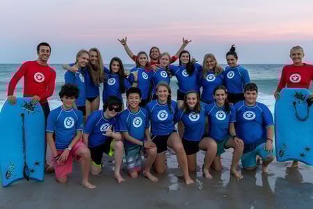 Estudiantes de la Bribie Island State High School con colorida ropa de surf en la playa al atardecer.