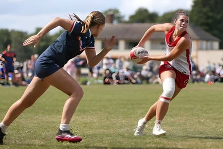 Dos deportistas de Brighton Girls luchan por el balón en el campo de fútbol frente a las gradas de espectadores.
