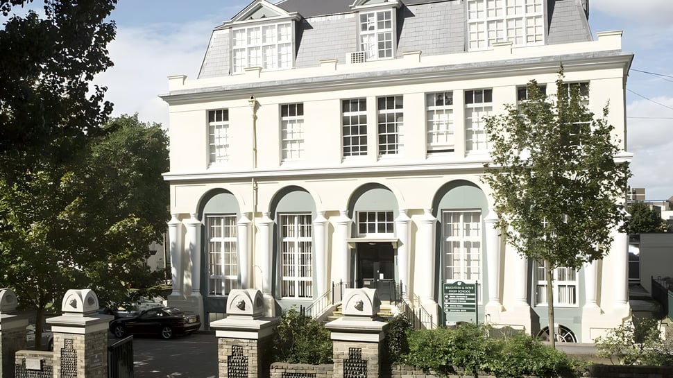 El edificio escolar histórico de Brighton Girls con ventanas de arco y una fachada decorativa rodeada de árboles.