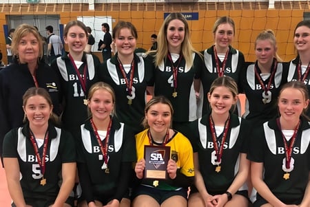 Un grupo de jóvenes jugadoras de voleibol posan en uniforme en el campo de voleibol de la Brighton Secondary School.