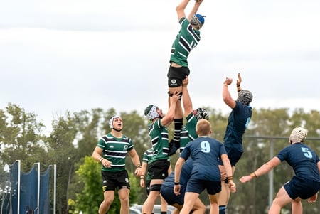 Un grupo de estudiantes que juegan al rugby del Brisbane Boys' College durante un partido con un jugador que salta alto para atrapar el balón.