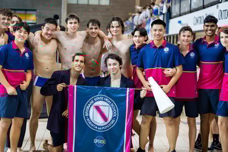 Un grupo de nadadoras y nadadores posan frente al banner de la Fédération Internationale de Natation en el campus de la Brisbane State High School.