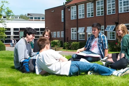 Estudiantes del Brockenhurst College están sentados en el césped frente al edificio de ladrillo y aprenden juntos.