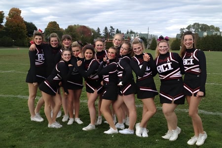Un grupo de jóvenes animadoras en uniformes negros y blancos está en el campo del Brockville Collegiate Institute.
