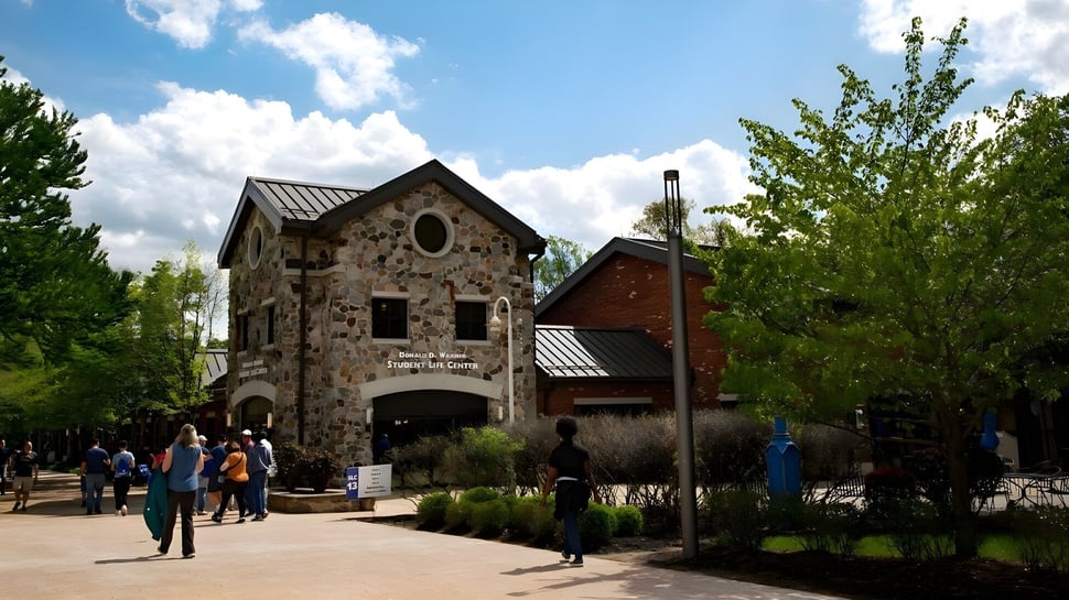 El edificio del Brookdale Community College está rodeado de vegetación verde y muestra una arquitectura típica bajo un cielo azul.