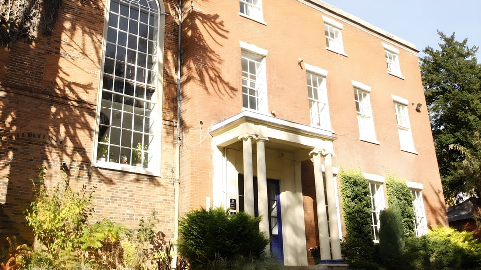 El edificio de ladrillo con grandes ventanas y entrada en el campus de Brooke House College está rodeado de áreas verdes.