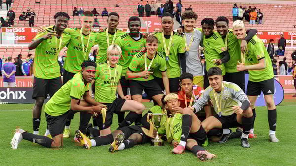 Estudiantes del Brooke House College celebran un gol en el campo de fútbol con espectadores en el estadio de fondo.