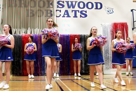 Estudiantes de la Brookswood Secondary School realizan cheerleading en una cancha de baloncesto con un cartel de Swood Cats al fondo.