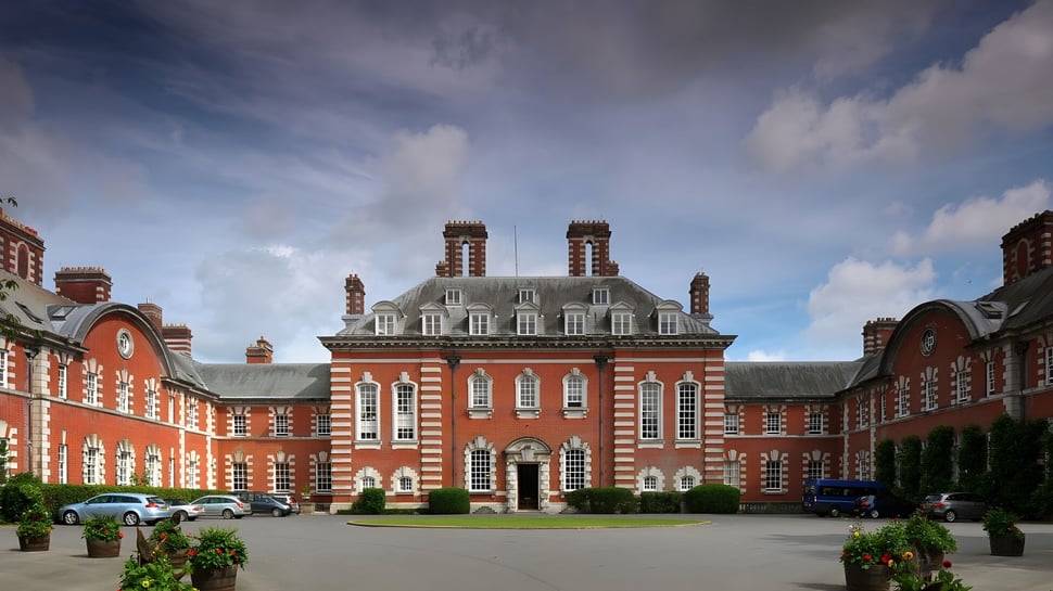 El edificio principal de la Bryanston School se encuentra en un patio plantado con vegetación circundante y coches estacionados.