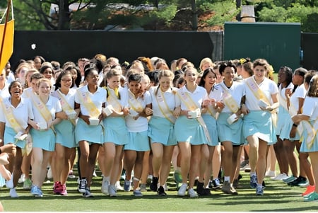 Un grupo de alumnas de The Bryn Mawr School está de pie en un prado con edificios y árboles al fondo.