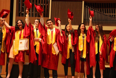 Un grupo de graduados de la Buckswood School está junto en togas rojas y amarillas sosteniendo sus diplomas en una ceremonia de graduación.