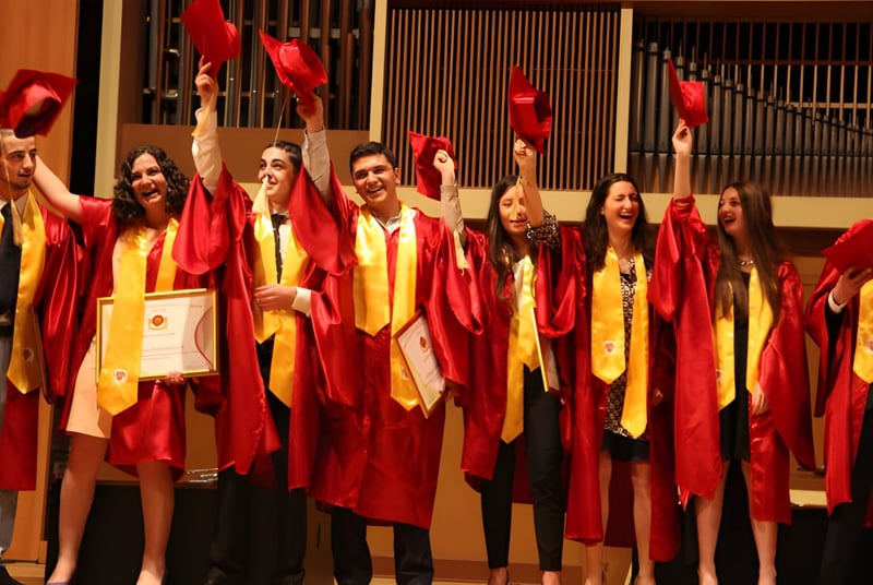Un grupo de graduados de la Buckswood School está junto en togas rojas y amarillas sosteniendo sus diplomas en una ceremonia de graduación.