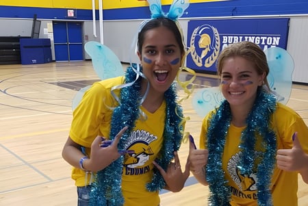 Dos alumnas de Burlington Central High School están con collares coloridos en el gimnasio frente a la cancha de baloncesto.