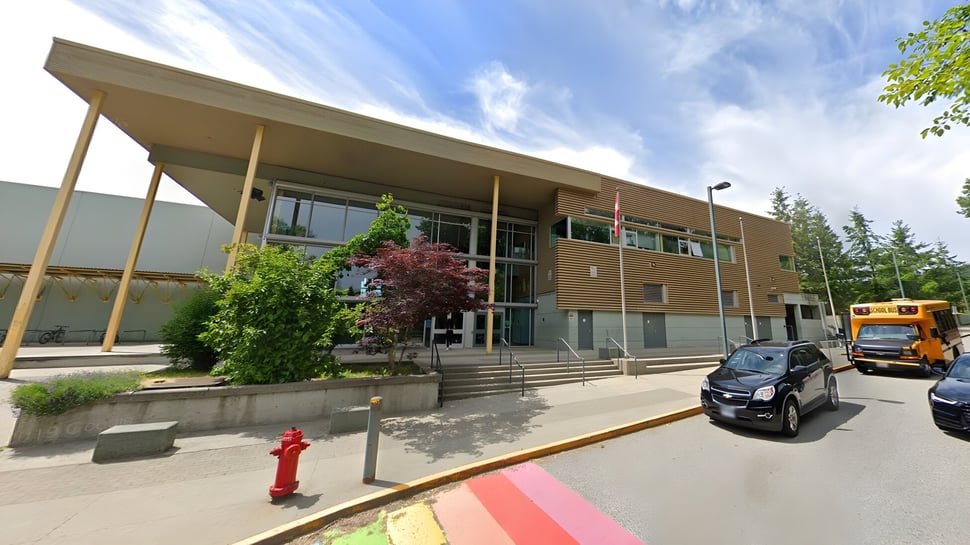 El moderno edificio de varios pisos de la Burnaby Mountain School con fachada de vidrio y entrada cubierta está rodeado de árboles.