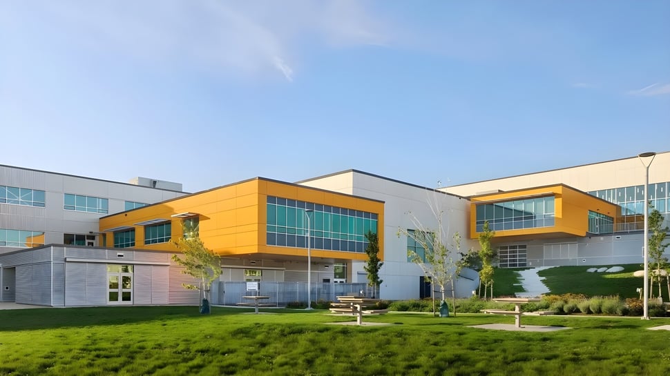 El moderno edificio de varios pisos de la Burnaby North School con fachada amarilla se encuentra en un césped bien cuidado rodeado de vegetación verde.