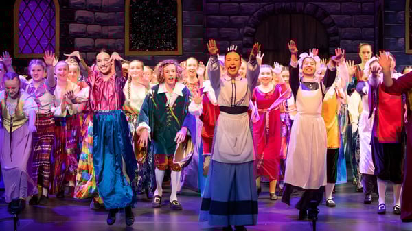 Estudiantes de la Burnie High School están en trajes coloridos en el escenario frente a un fondo de piedra medieval.