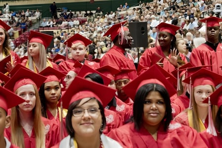 Las graduadas y graduados de la Burnie High School están juntos en túnicas rojas durante una ceremonia de graduación.