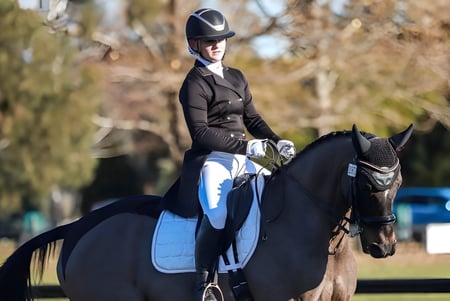 Una estudiante de Burnside High School monta un caballo negro al aire libre con árboles de fondo.