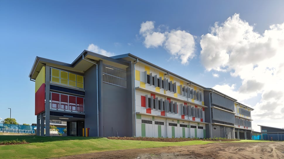 El edificio de varios pisos del Burpengary State Secondary College muestra una fachada colorida frente a un cielo azul y un prado verde.