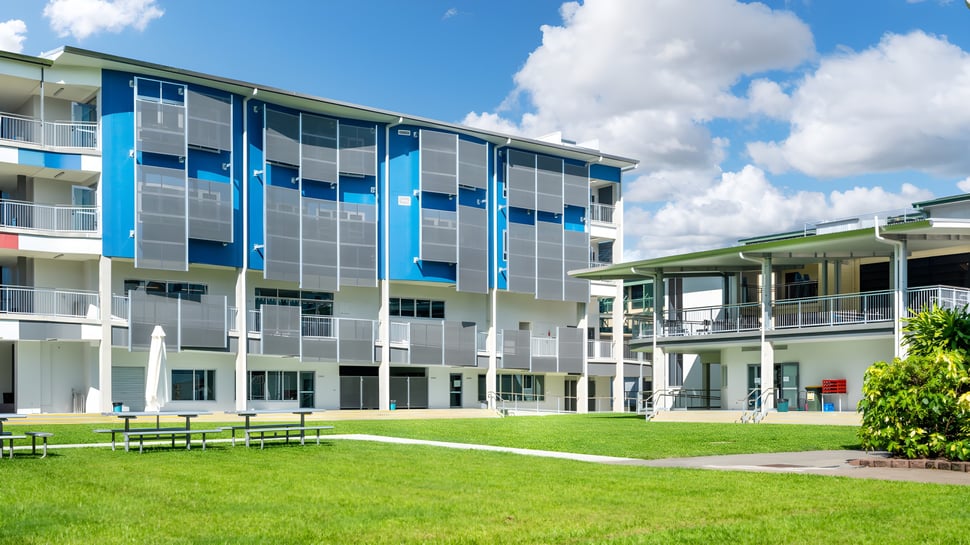 El moderno edificio de varios pisos de la Bush Post Primary School está rodeado de una superficie de césped y árboles.
