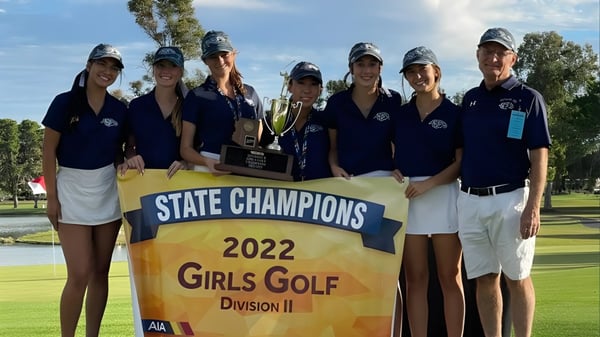 Un grupo de alumnas de la Cactus Shadows High School sostiene un trofeo frente a un banner de las Campeonas Estatales 2022 en golf femenino.