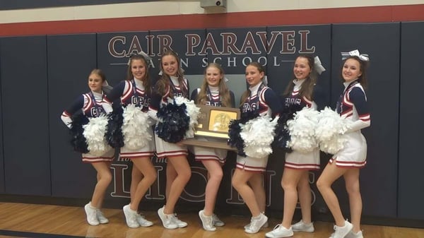 Un grupo de estudiantes de la Cair Paravel Latin School está en uniformes uniformes frente a una pancarta escolar.