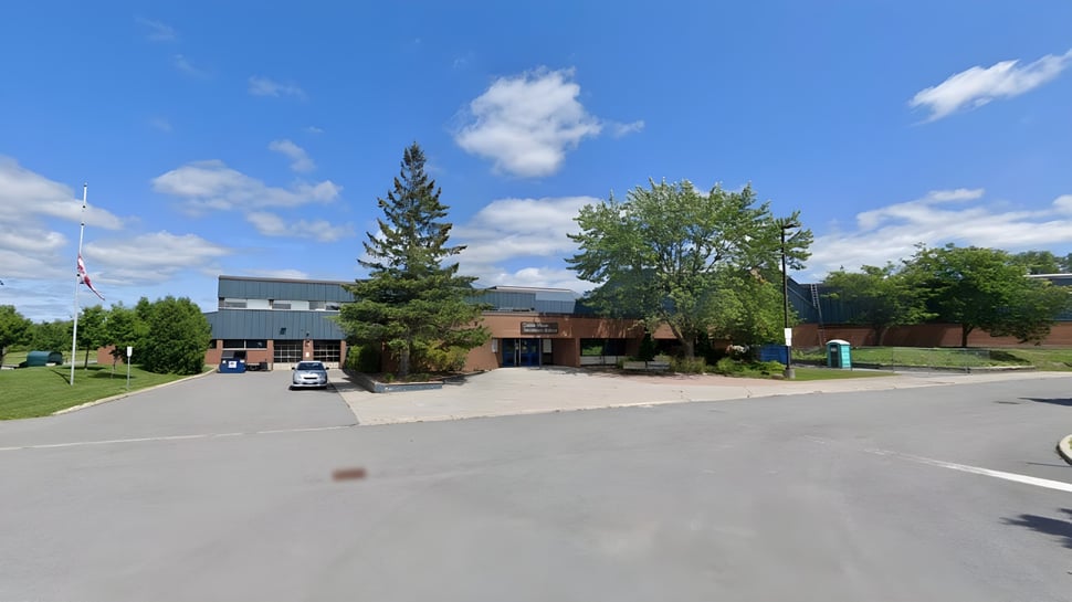 El moderno edificio de varios pisos de la Cairine Wilson Secondary School con un gran estacionamiento y rodeado de árboles bajo un cielo azul.