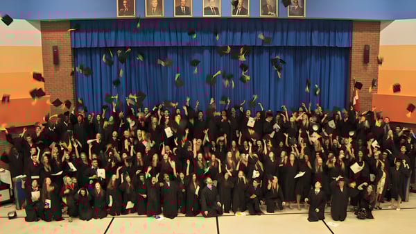 Los graduados de la Cairine Wilson Secondary School celebran su graduación frente a un escenario con cortinas azules.