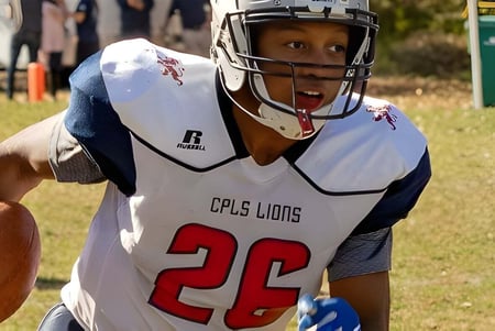 Un joven jugador de fútbol americano de la Cair Paravel Latin School está de pie con casco y balón en el campo.