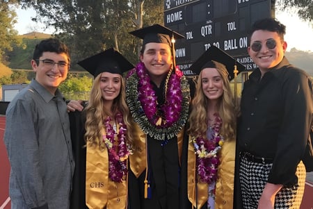 Un grupo de graduados está en vestimenta académica frente a un logo en el campus de la Calabasas High School.