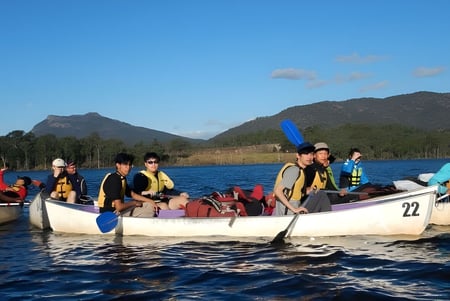 Estudiantes del Calamvale Community College realizan un paseo en bote en un lago de montaña bajo un cielo azul.