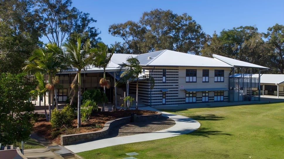 El edificio de madera de dos pisos con techo de metal de Caloundra State High School está rodeado de exuberante vegetación y palmeras.