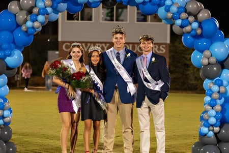 Un grupo de cuatro personas está frente a un arco de globos en el campus de la Calvary Day School.