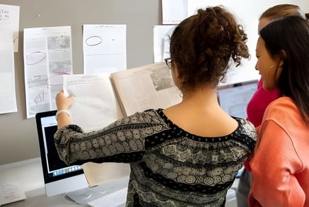 Dos estudiantes de la Cambridge Rindge and Latin High School están frente a una pizarra y discuten documentos juntos.